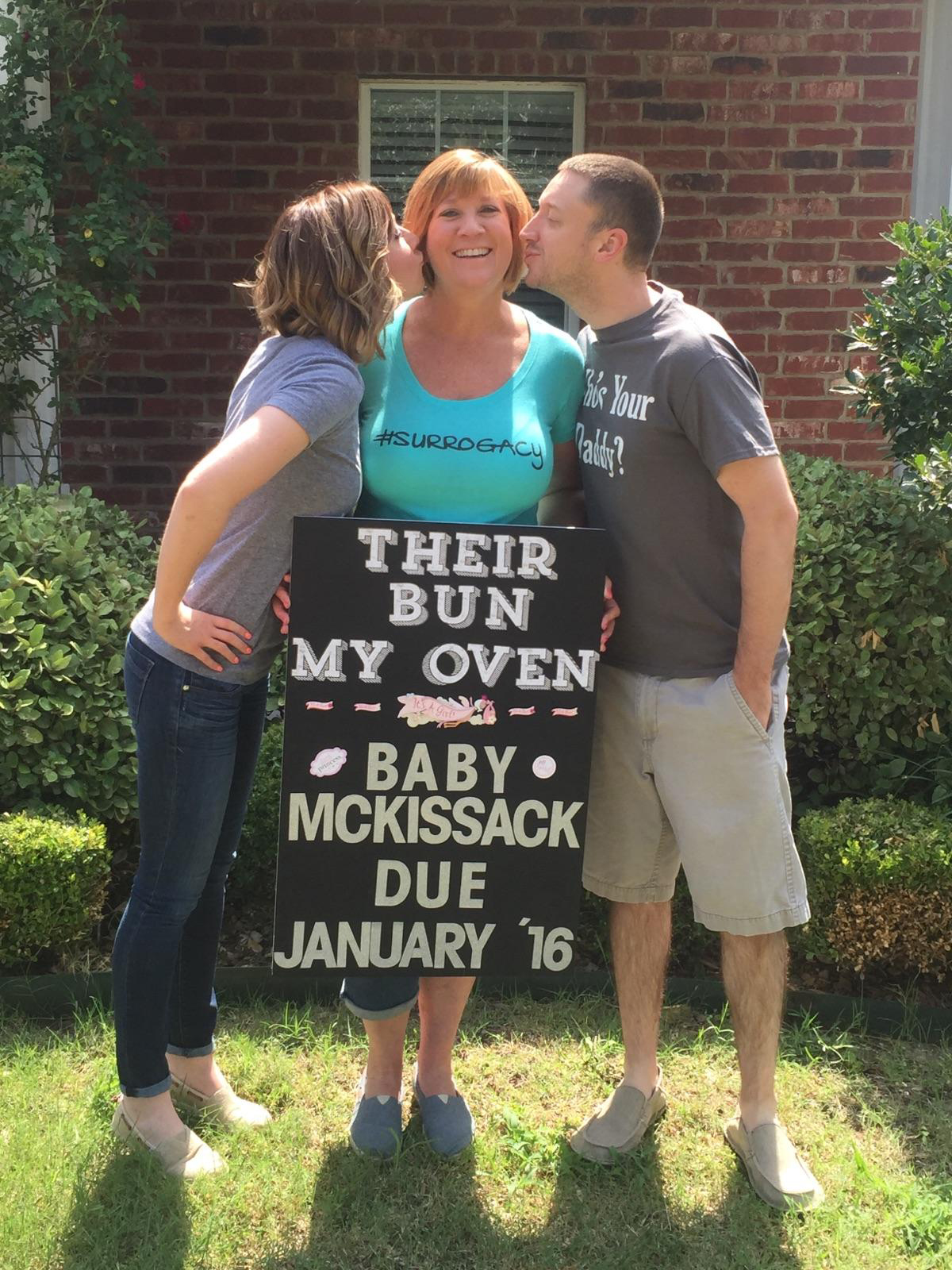 Woman and man kissing woman on cheek with sign that says Their Bun My Oven Baby McKissack Due January 16