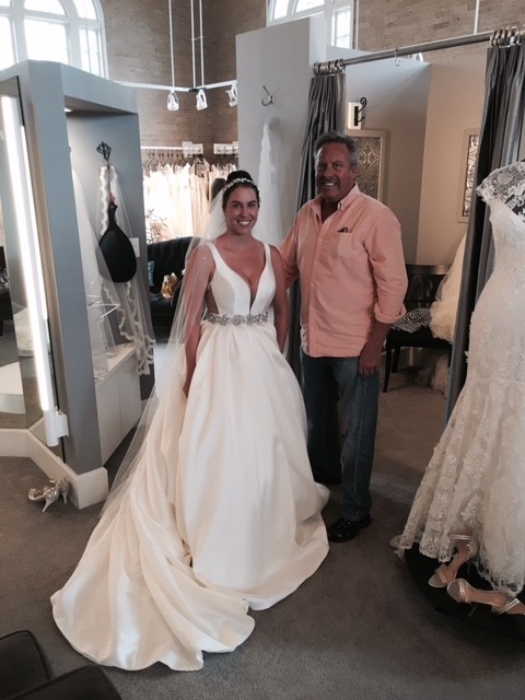 Woman wearing wedding dress posing with father at bridal store