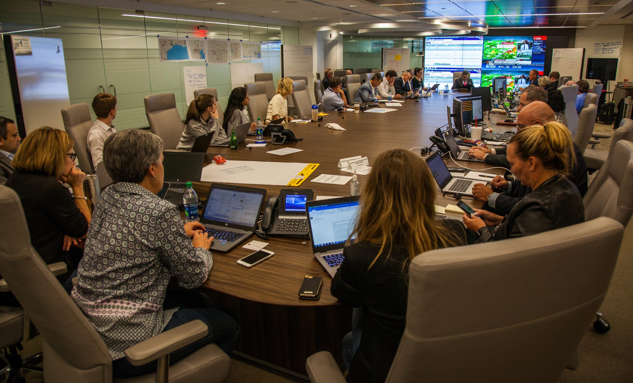 People sitting around large conference table looking at screens with hurricane information