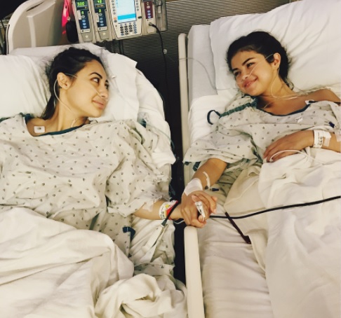 Two women lying in hospital beds and holding hands