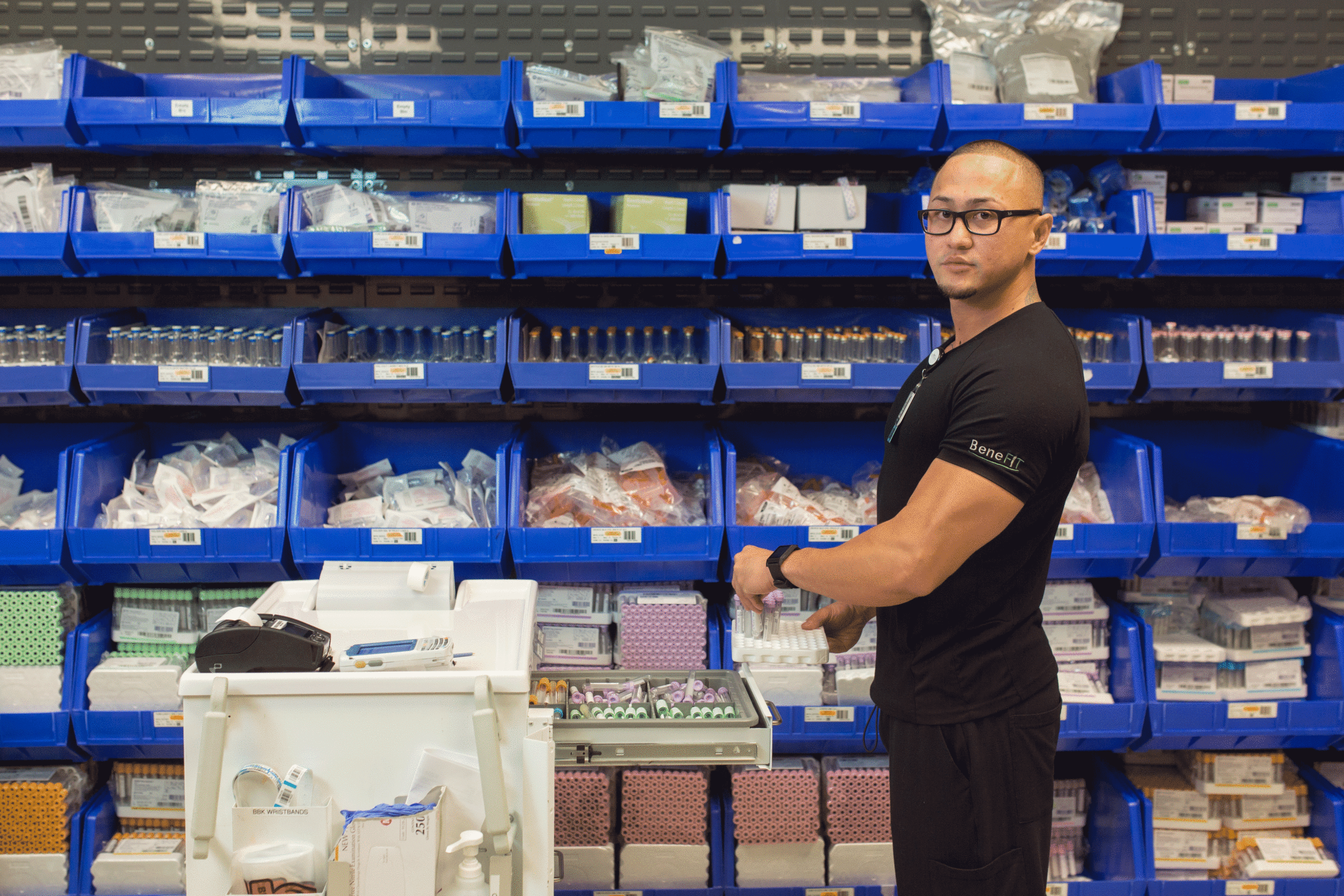 Man wearing black scrubs standing in front of shelves of medical supplies