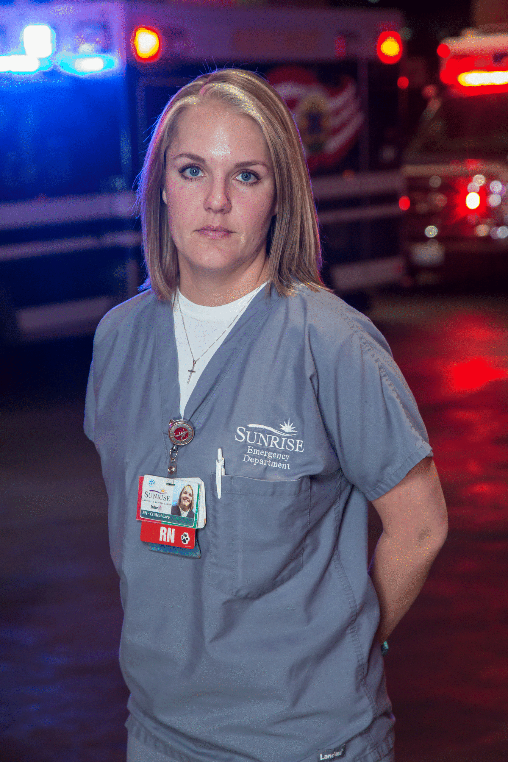 Female nurse with red and blue emergency lights behind her