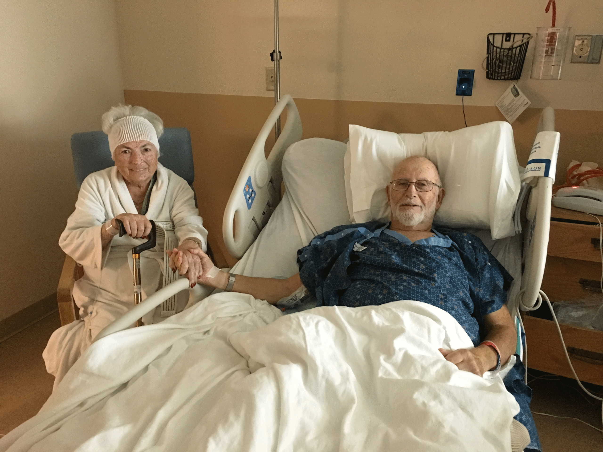 Man in hospital bed holding hands with woman sitting next to him