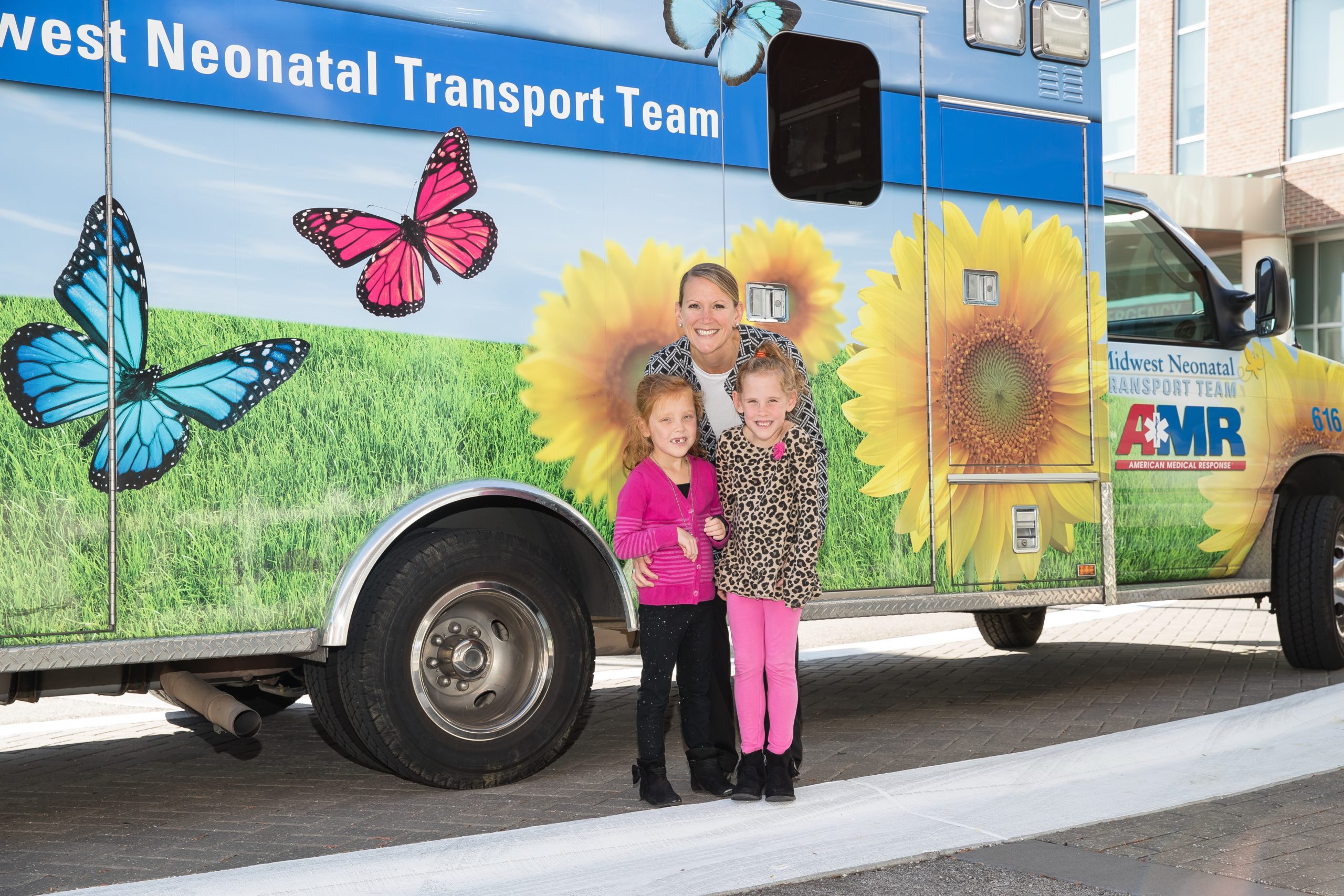 Woman and two girls standing next to neonatal transport ambulance