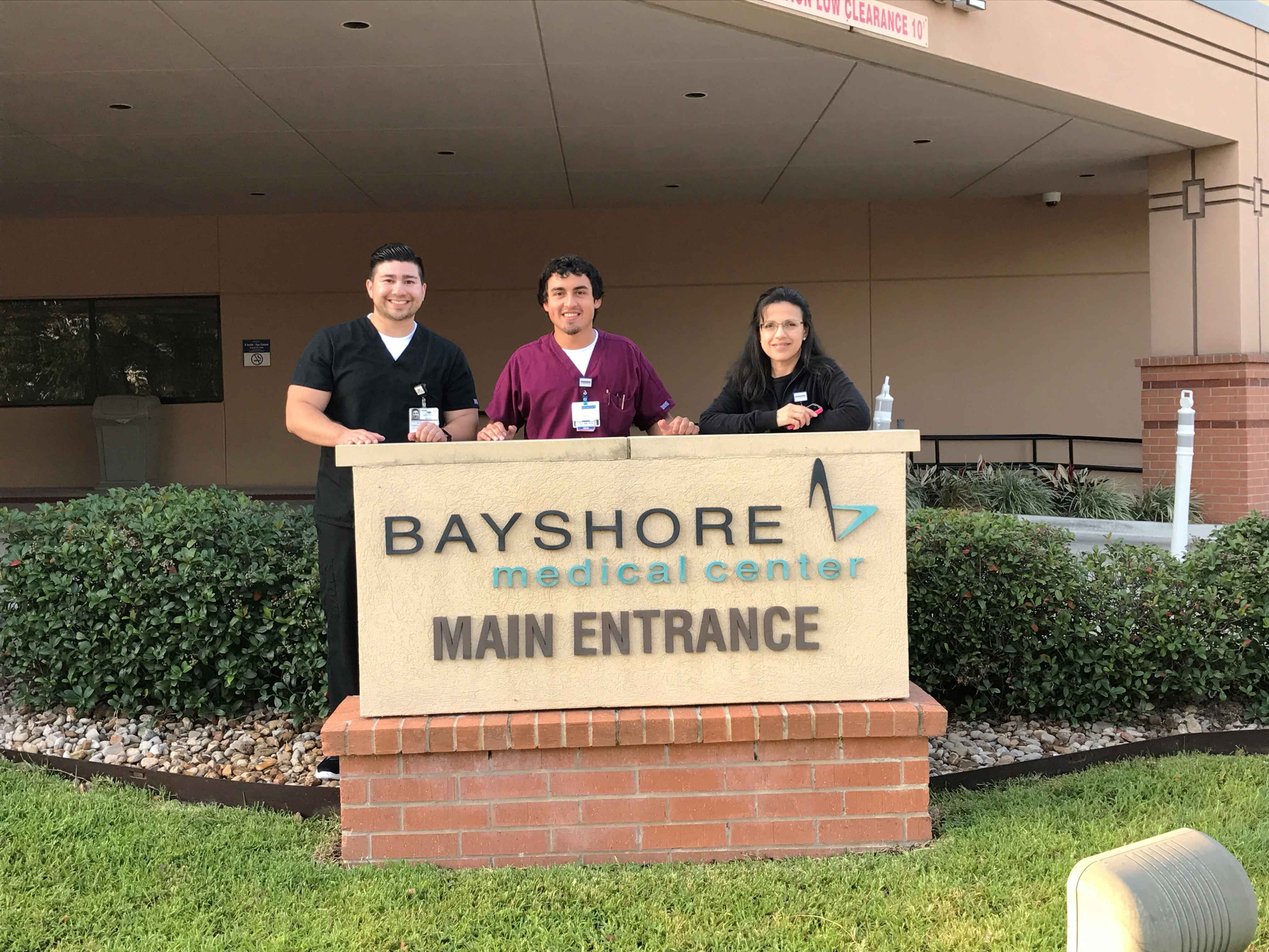 Three hospital caregivers standing behind Bayshore Medical Center's Main Entrance sign