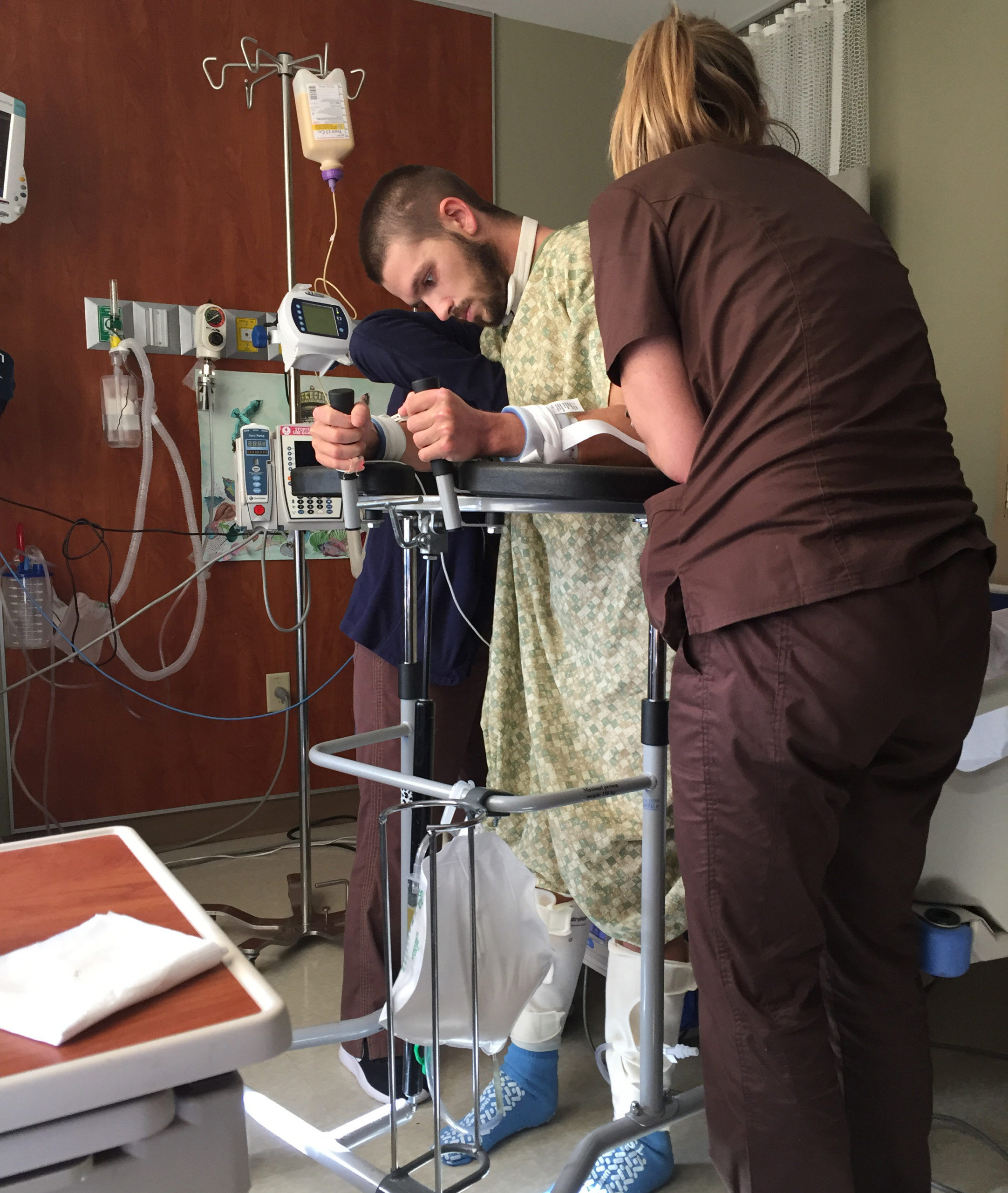 Male hospital patient holding onto stand as nurses help him stand up