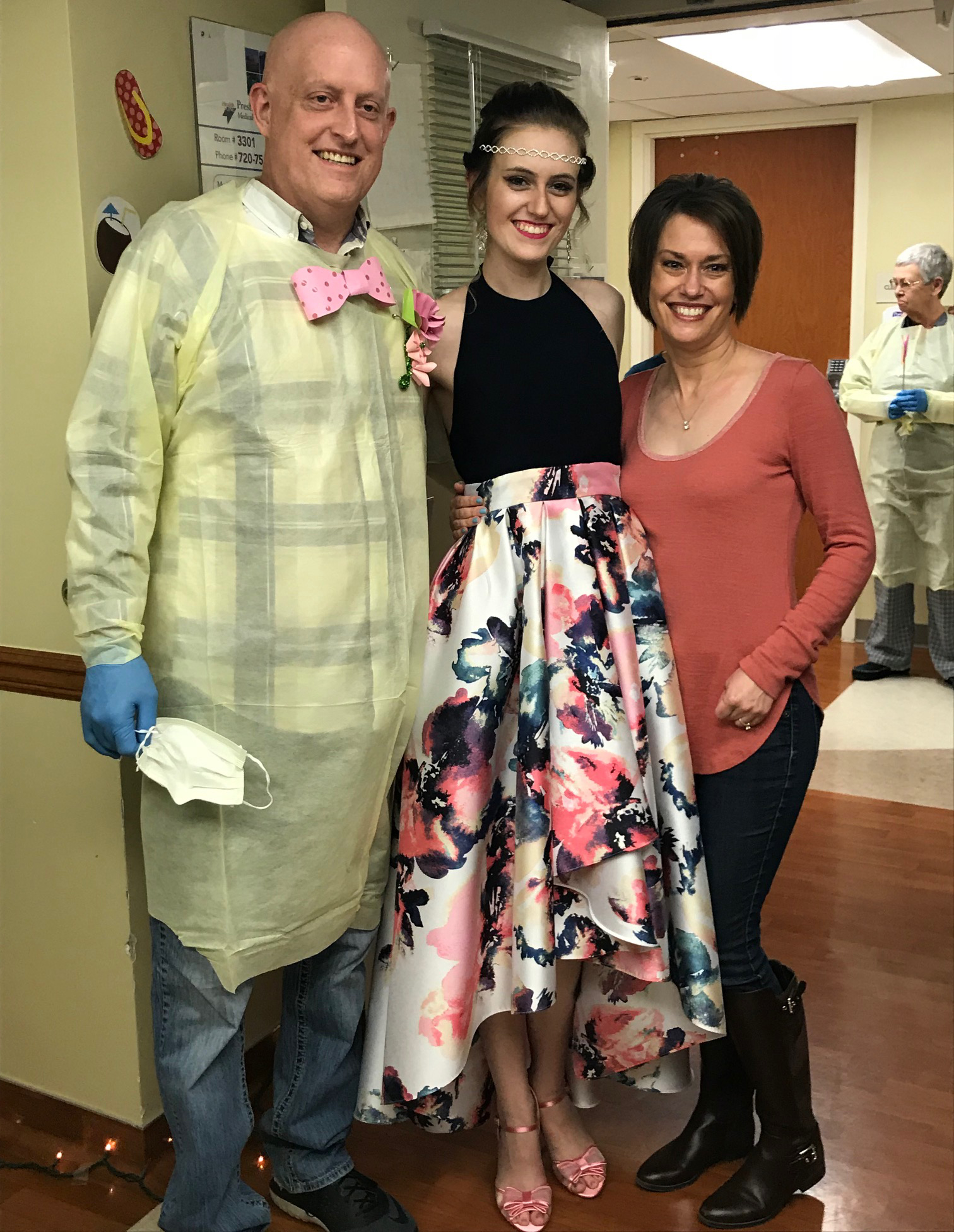 Girl wearing prom dress posing for a photo with her parents in hospital room