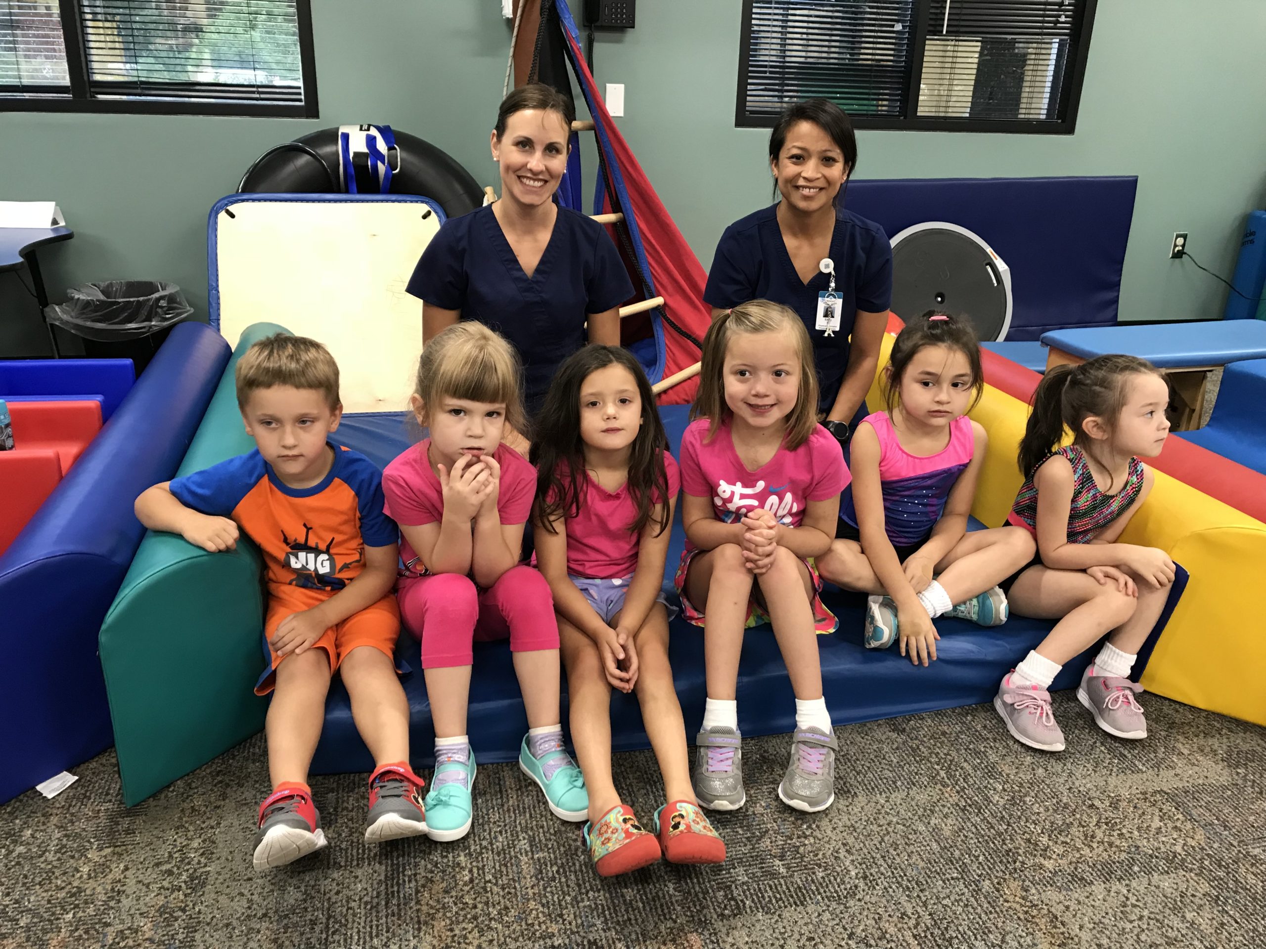 Two female physical therapists posing with a group of kids during a yoga class