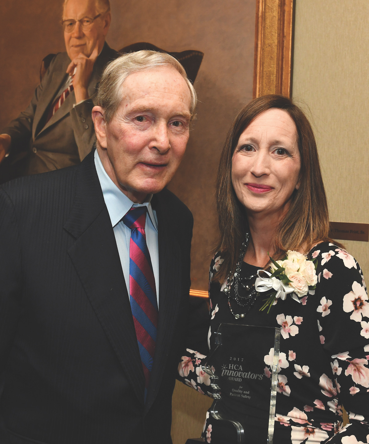 Man in suit and tie with woman in floral dress holding award