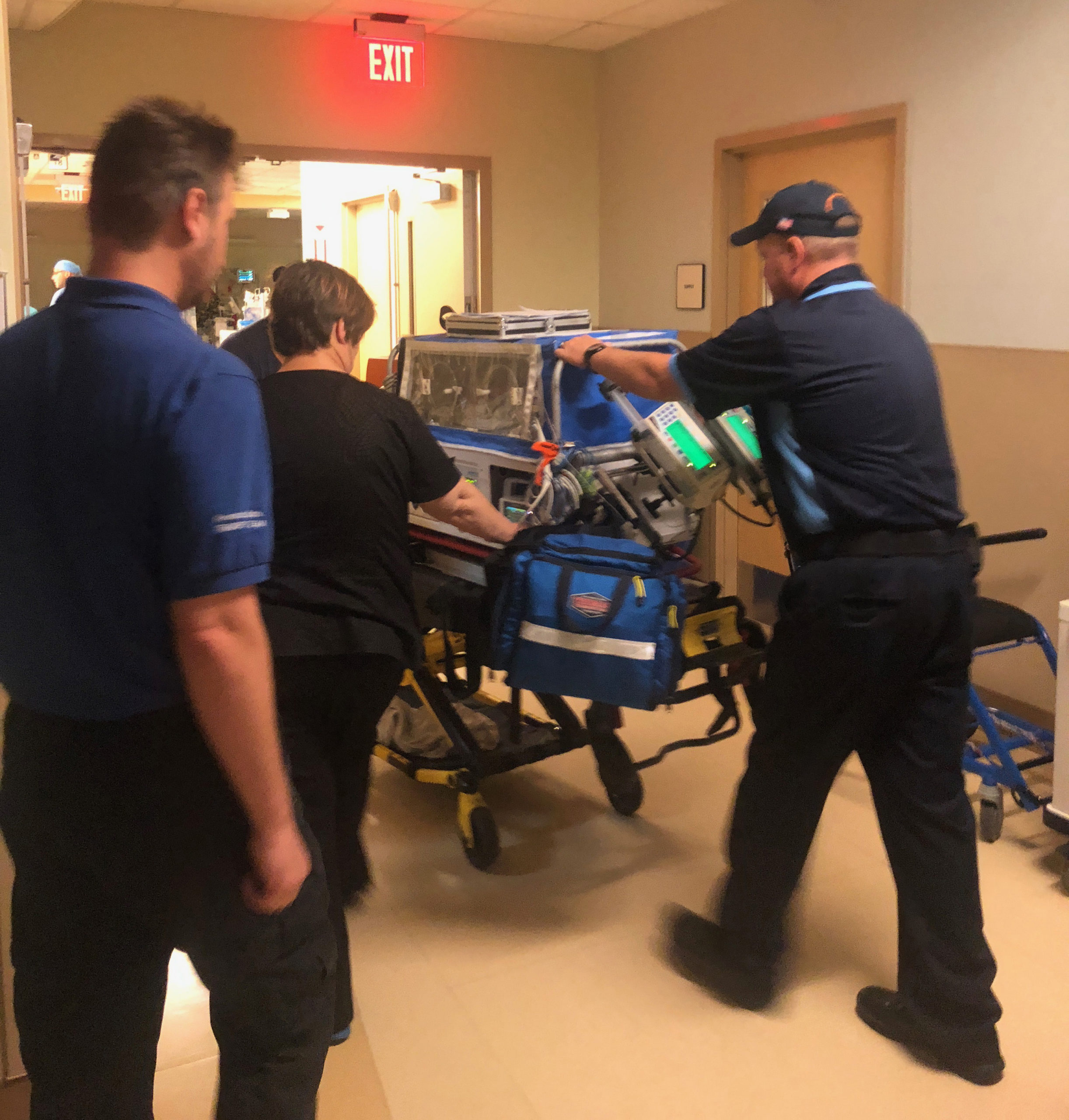 Team of caregivers transporting baby in incubator down hospital hallway