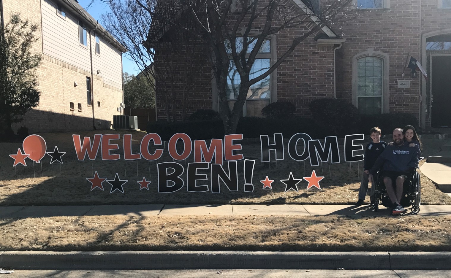 Man and children posing with lawn sign that says Welcome Home Ben
