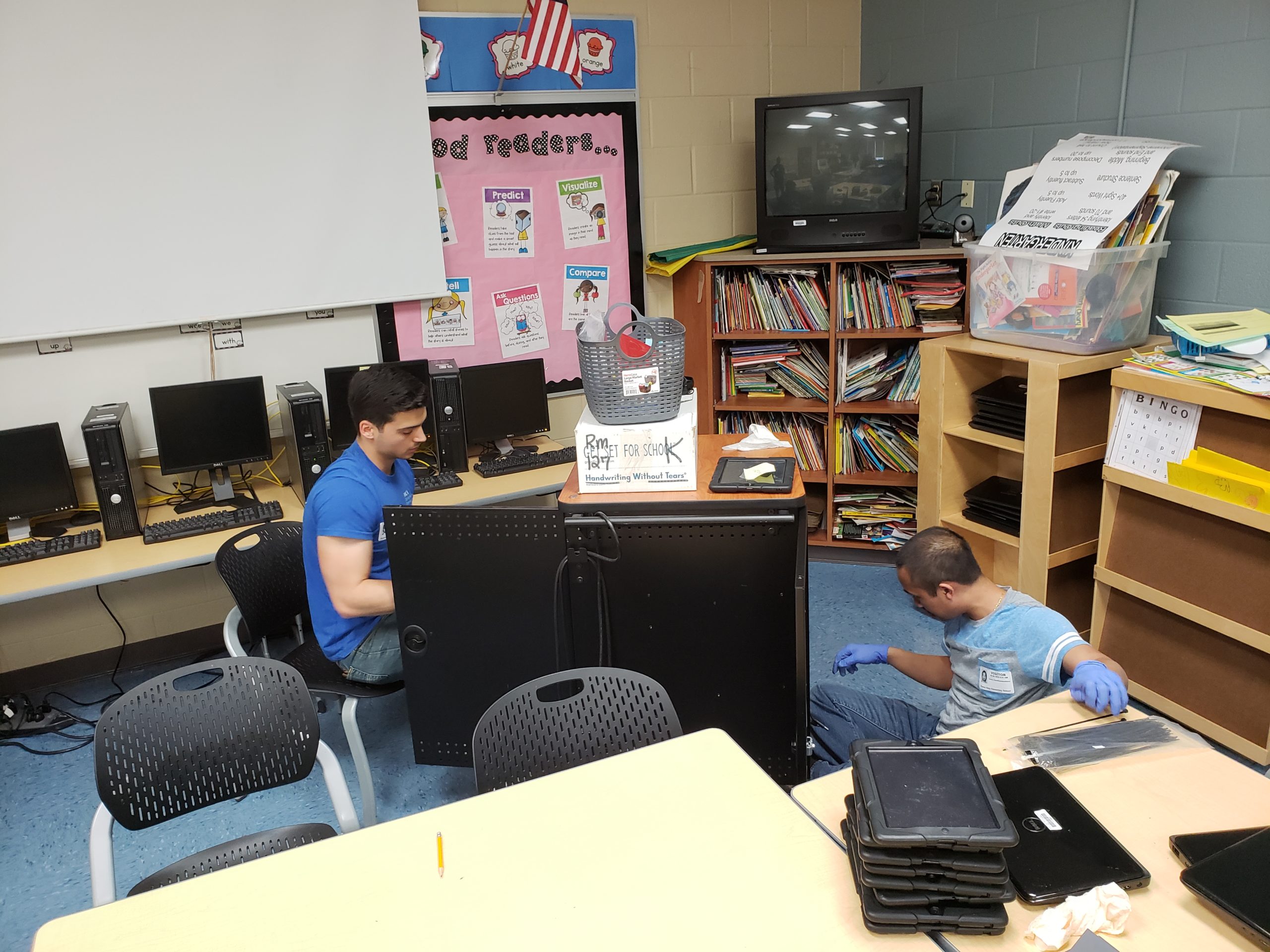Two male volunteers working with TVs, computers and tablets
