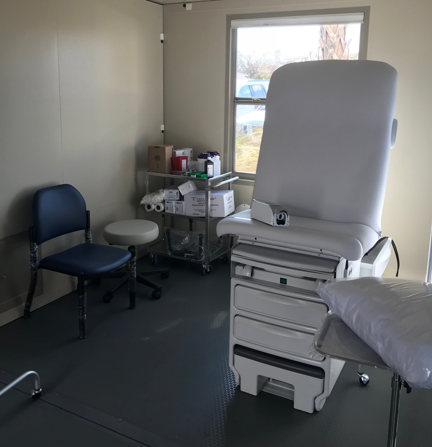 Room with small hospital bed, chairs and medical supplies