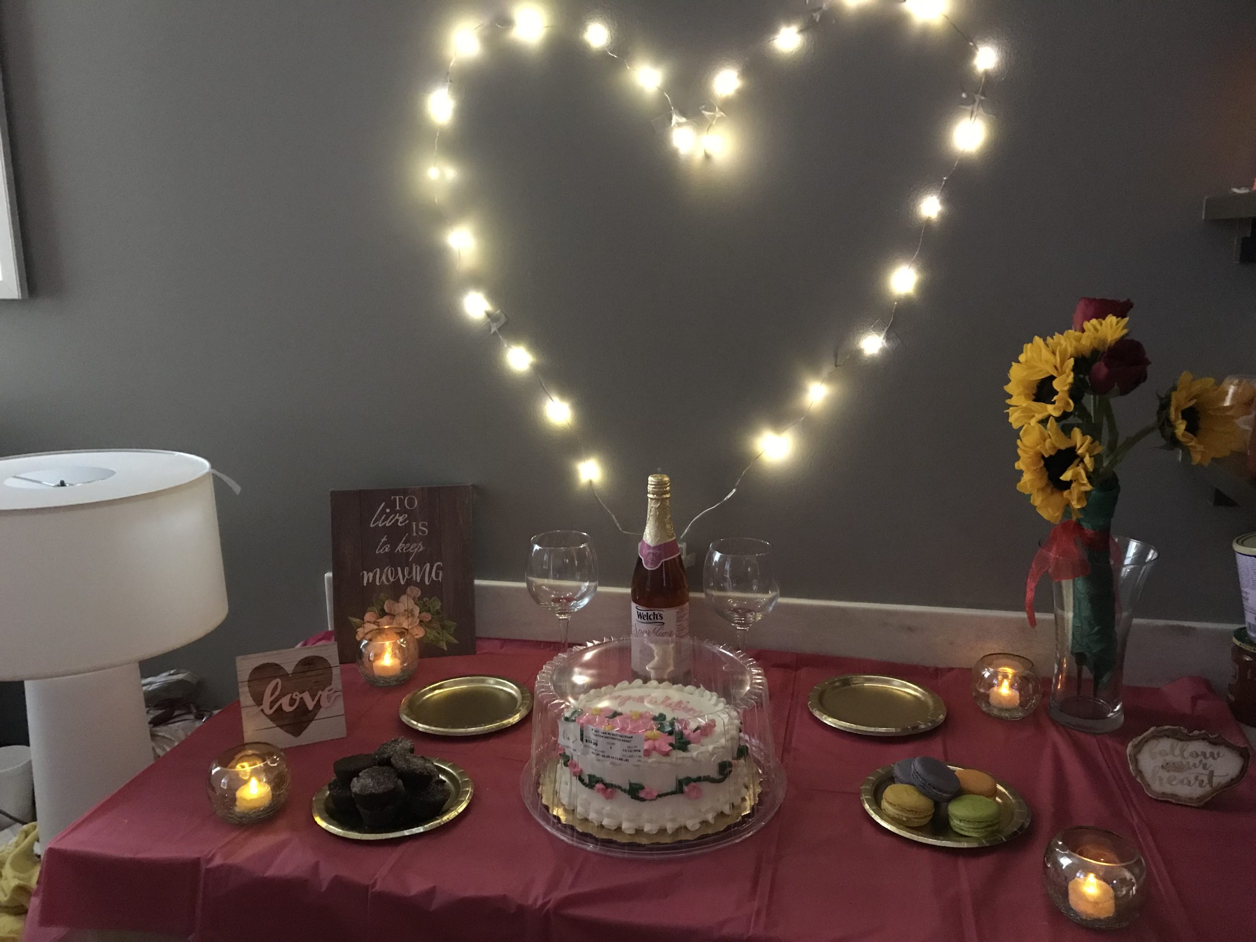 A string of lights making a heart shape behind a table with flowers and desserts