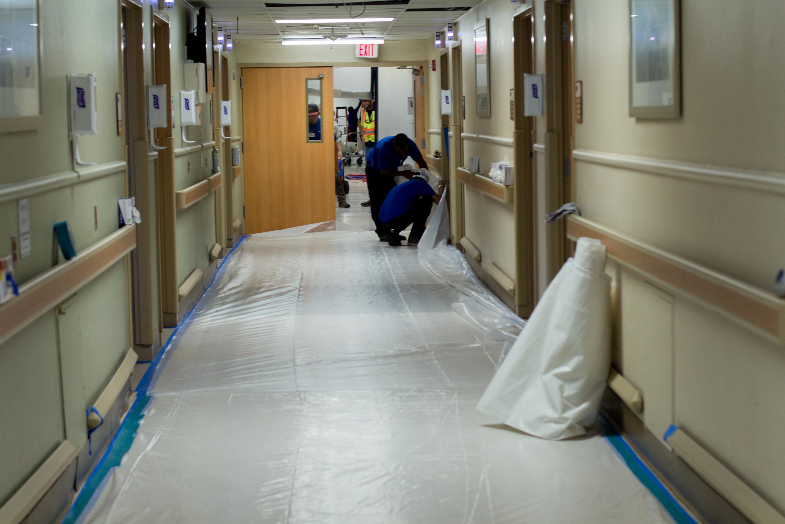 Hospital workers taping plastic sheet along hallway floor