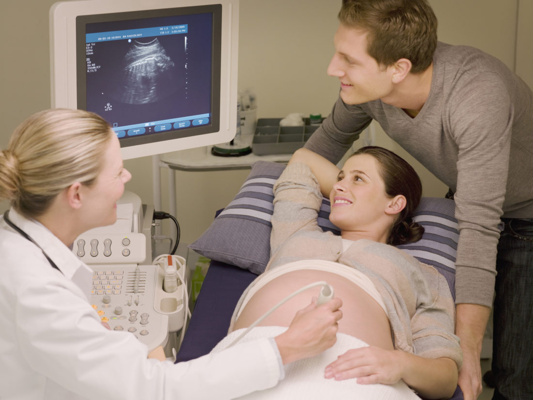 A female doctor performing an ultrasound on a pregnant woman who is looking at the monitor along with her male partner