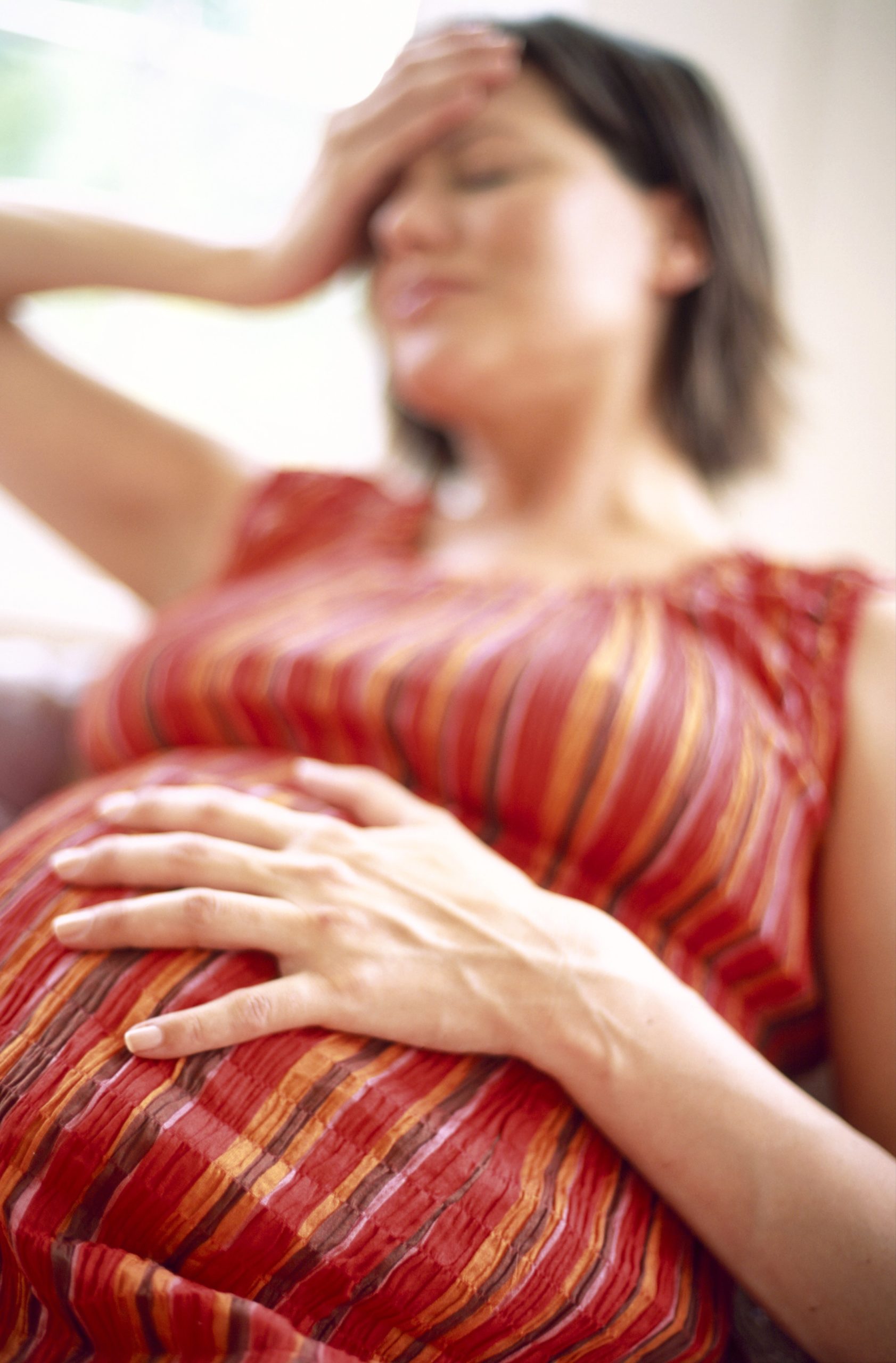 Pregnant woman with one hand on her belly and one hand on her forehead