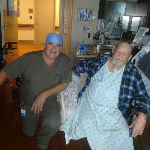 Male doctor in scrubs and surgical cap kneeling next to male patient in hospital bed