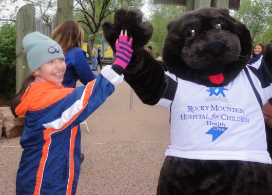 Teenage girl high-fiving mascot wearing a Rocky Mountain Hospital for Children t-shirt