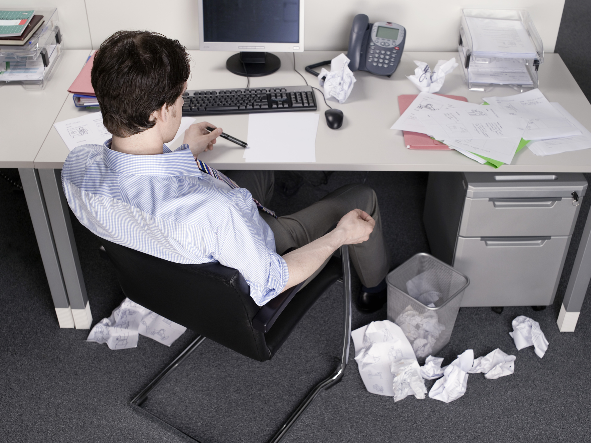 Man sitting at desk with crumpled-up papers littering the ground around him
