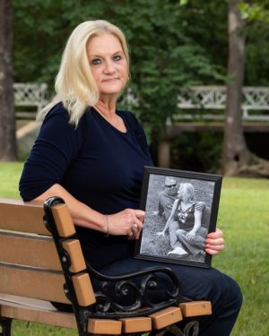 Sheri Tolbert sitting on a park bench, holding a framed photo 