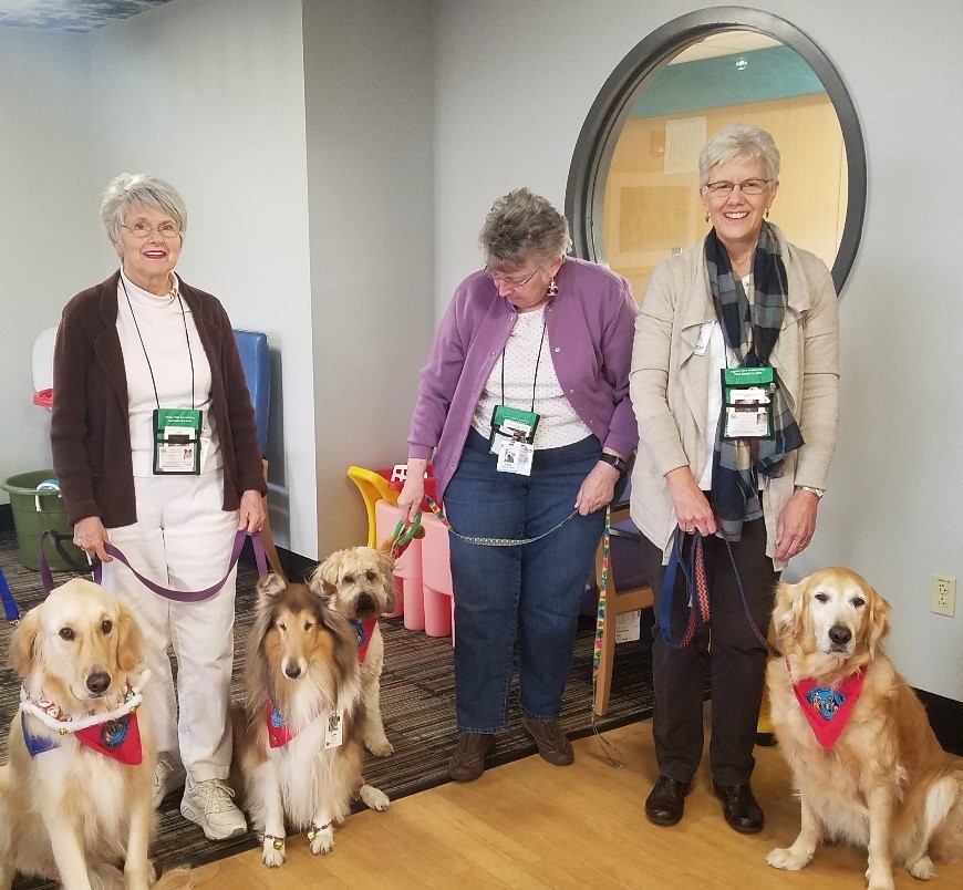 Three women stand with four dogs indoors