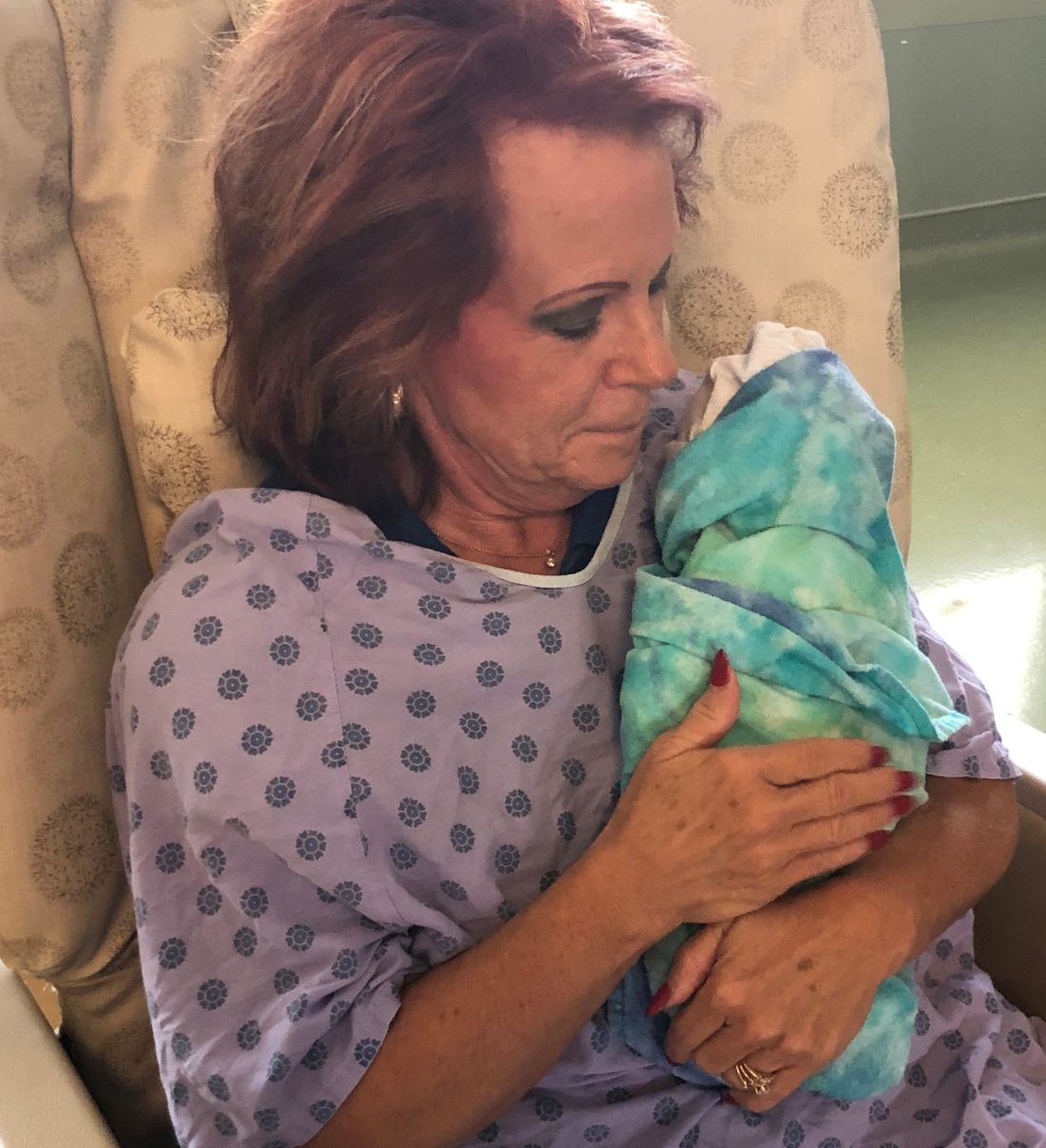 Woman wearing hospital gown and holding swaddled baby