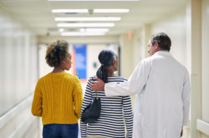 A male doctor talks with two female patients as they walk down a hospital hallway