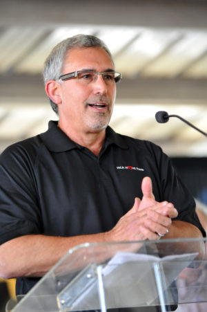 A man in a black polo speaks at a podium