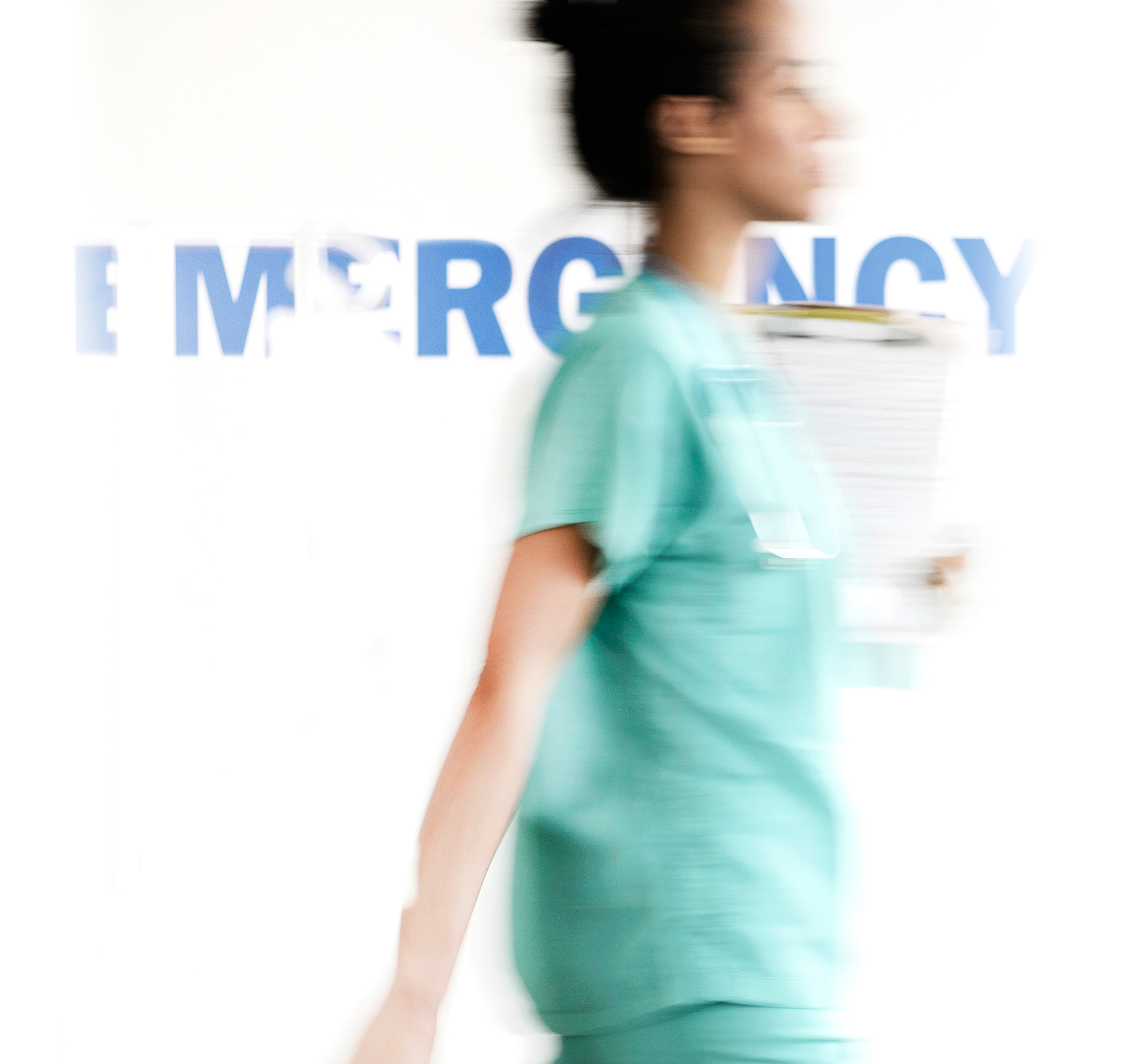 Healthcare professional walking past a wall that says "EMERGENCY"