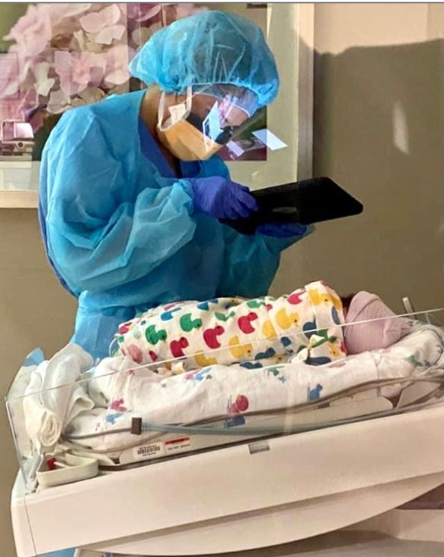 Medical professional in personal protective equipment using iPad to take photo of newborn baby 