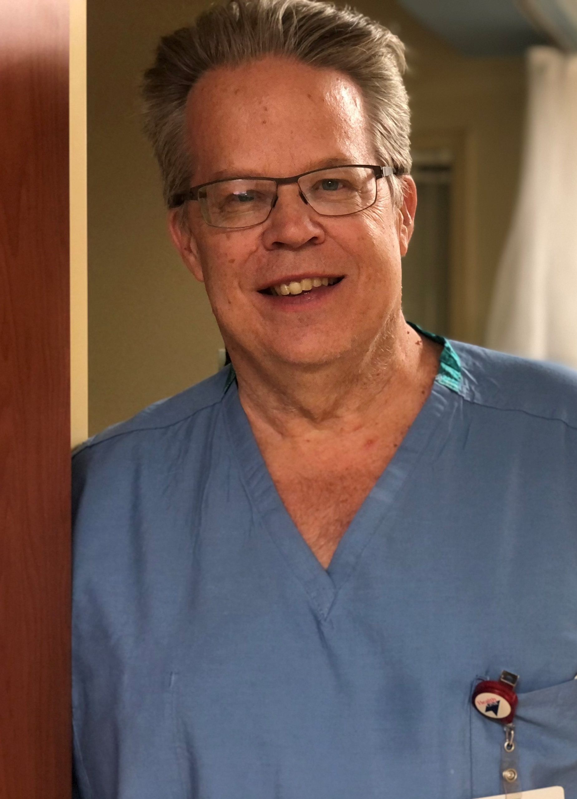 Man wearing glasses and blue scrubs. Headshot of Dr. Thomas Heffron.