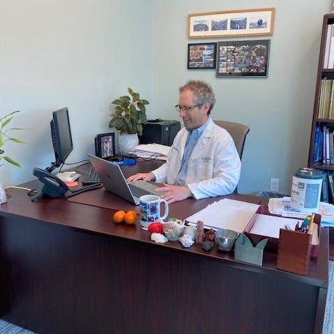 Dr. Alan Schulman sits at his desk  with a laptop