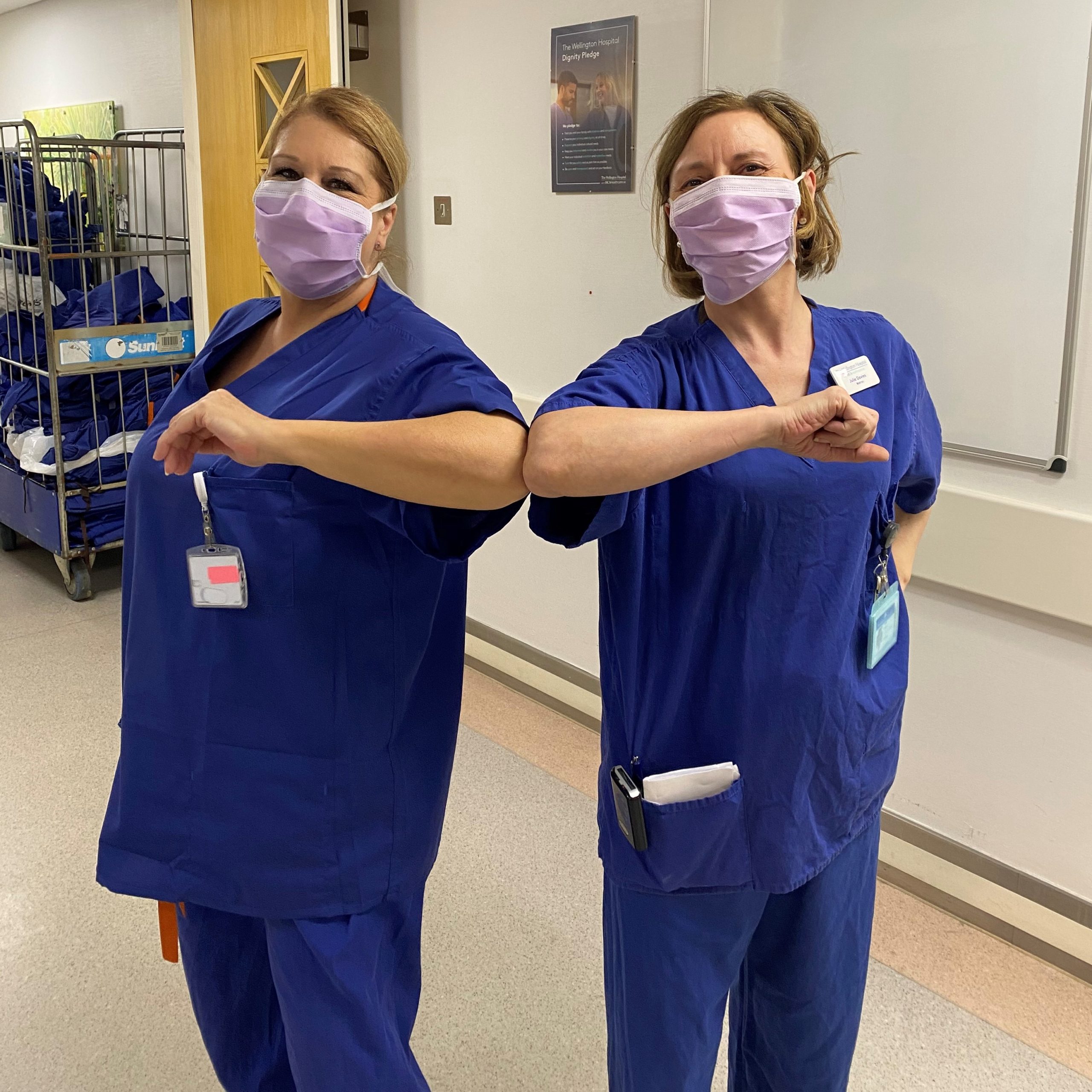 Two female nurses wearing face masks and bumping elbows 