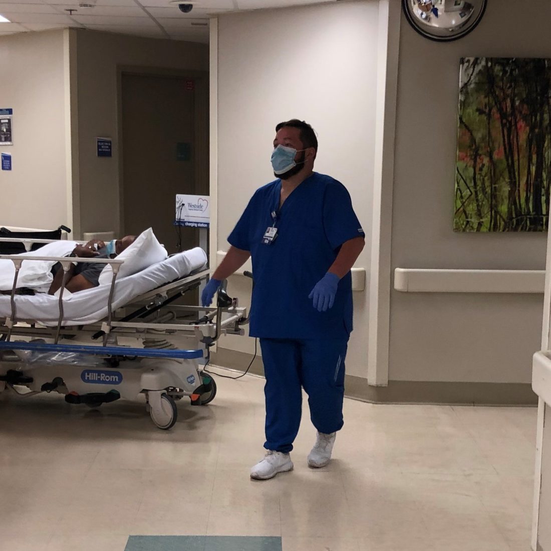 Patrick Pabone in scrubs, a protective face mask and gloves walking through a hospital hallway