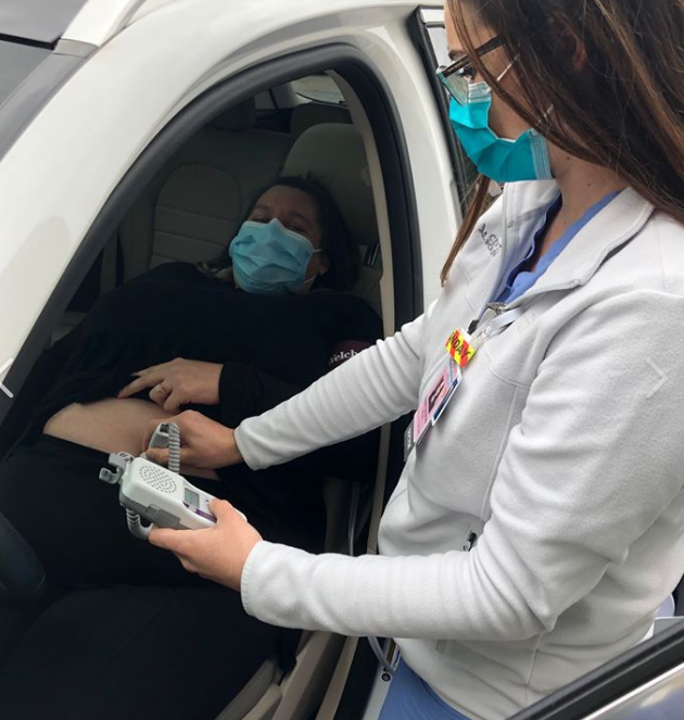 Female medical professional standing and performing an ultrasound on a pregnant woman who is seated in the driver's seat of her parked car with the door open