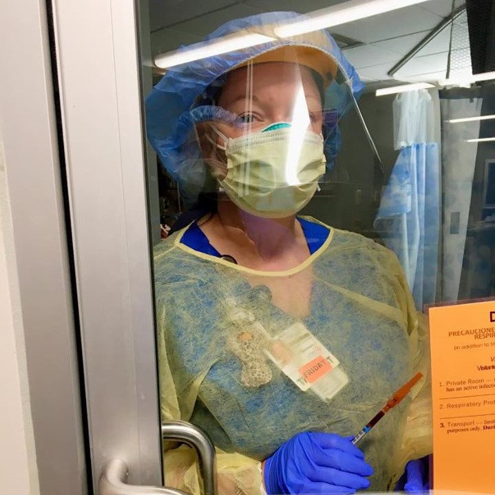 Tiffany Wimberly wearing personal protective equipment and clothing over her scrubs, standing behind a glass door