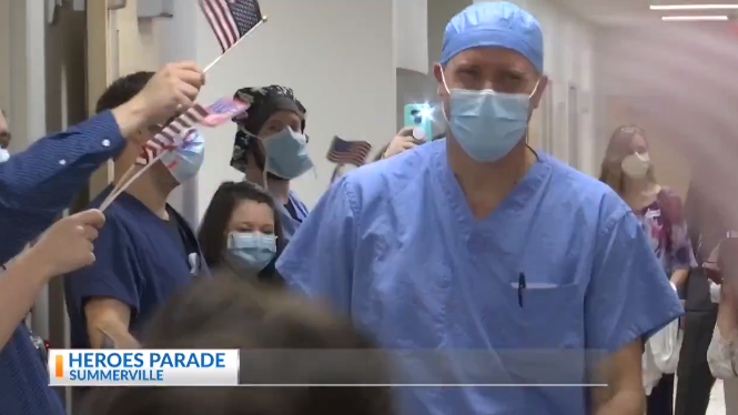 Dr. Eric Stem wearing hospital scrubs and a protective face mask walking past other adults in hospital scrubs and masks waving American flags. Caption says, "HEROES PARADE SUMMERVILLE"