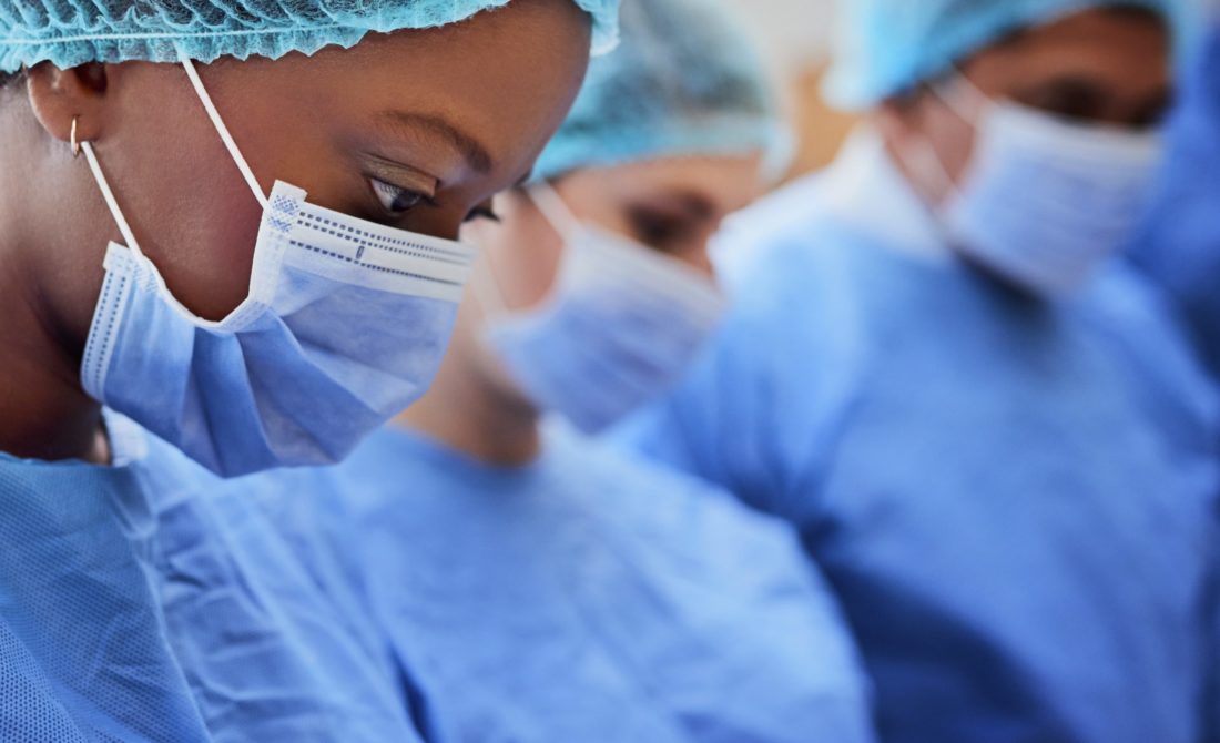 Three surgeons wearing surgical gowns and face masks