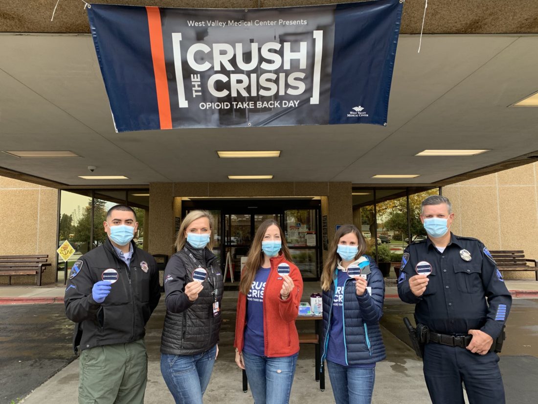 Five people wearing face masks standing in front of a Crush the Crisis sign
