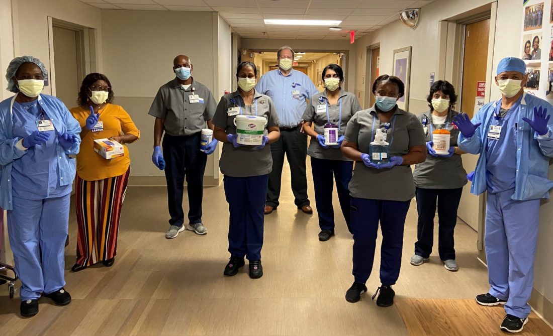 A group of nine environmental services employees standing in a hospital hallway