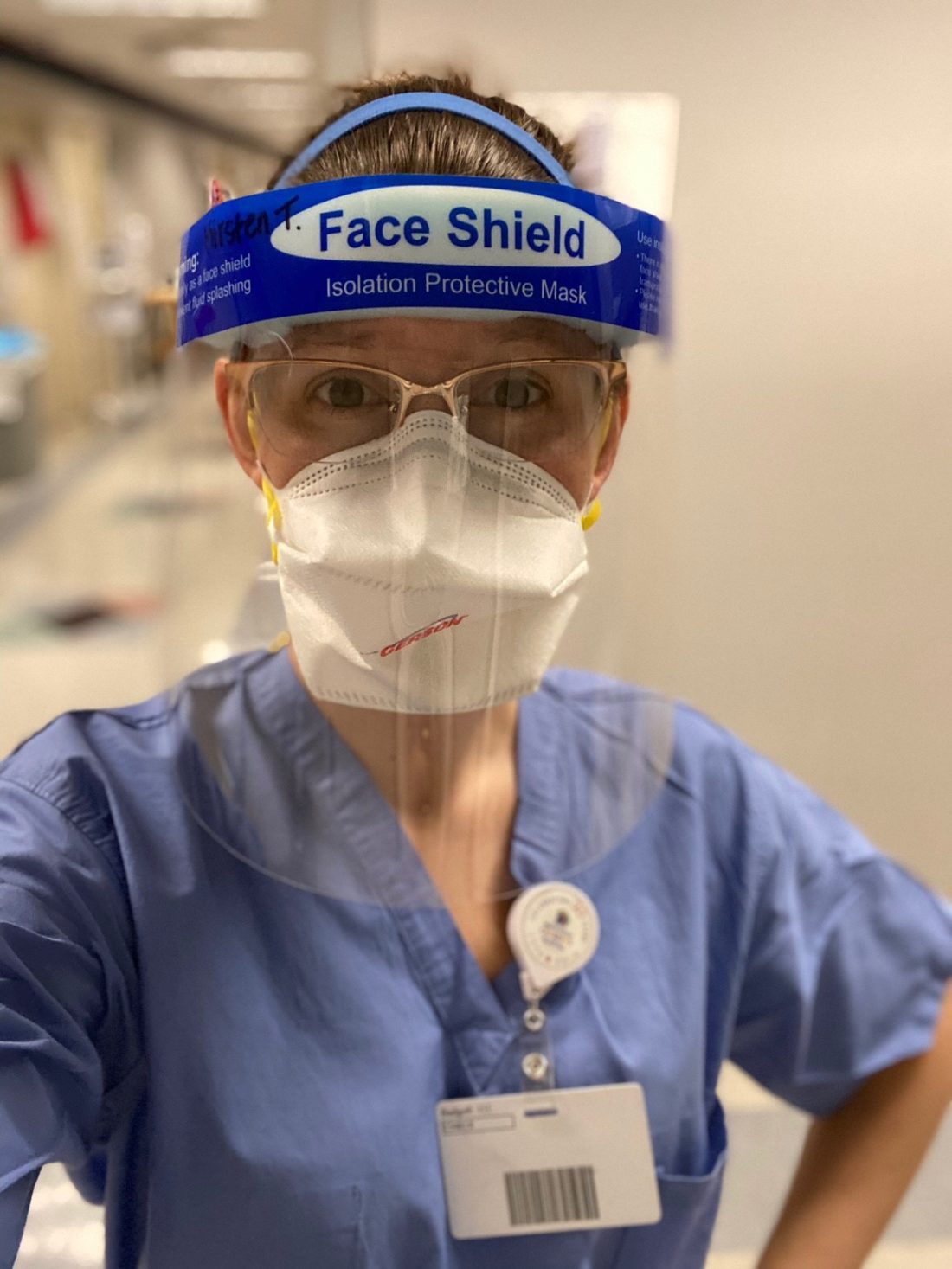Female nurse wearing blue scrubs, a face mask and face shield 