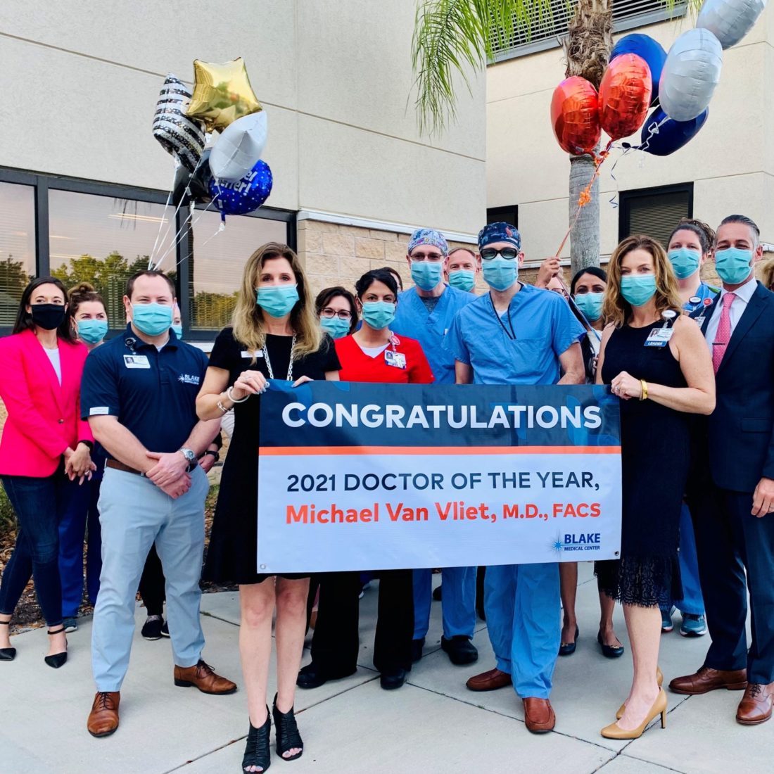 A group of hospital workers standing outside with a sign that says Congratulations, 2021 Doctor of the Year, Michael Van Vliet, MD, FACS