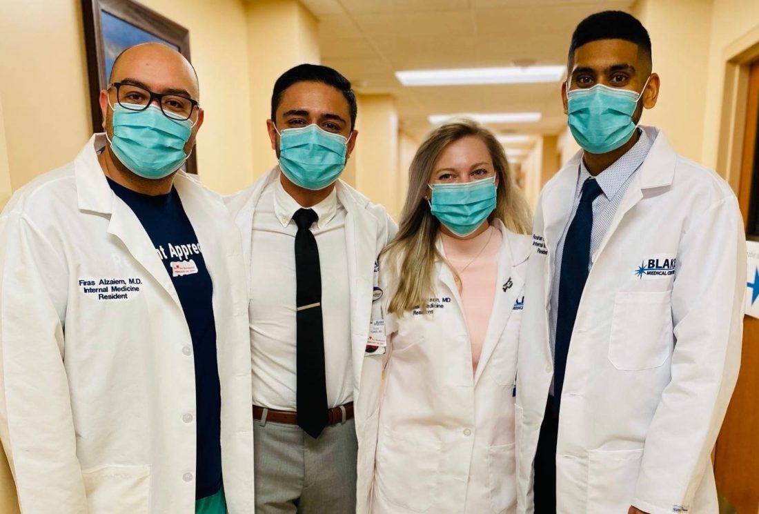 Four resident physicians wearing white lab coats and face masks. 