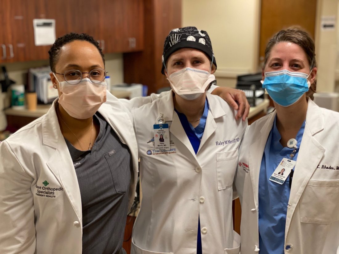 Three female doctors wearing white lab coats and face masks. 