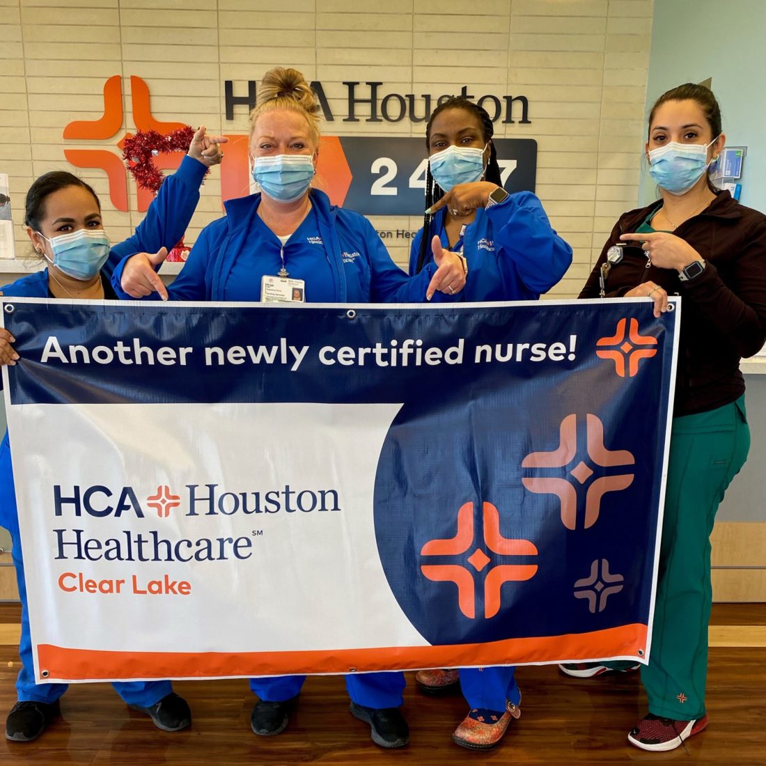 Four female nurses holding a sign celebrating a newly certified nurse. 
