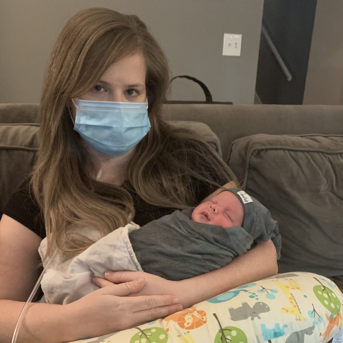 Woman wearing face mask holding newborn baby. 