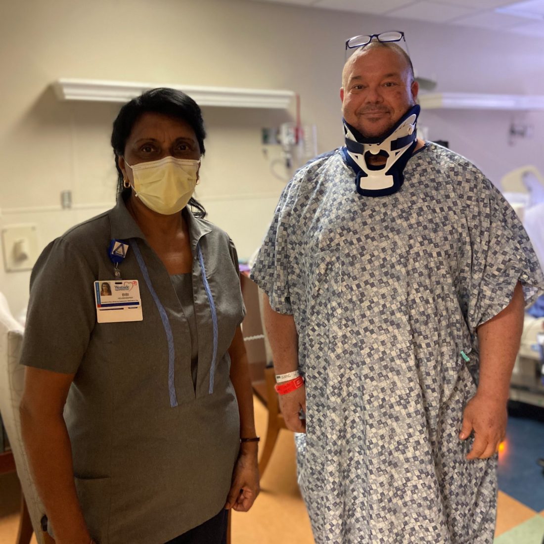 Female hospital worker standing with a male patient in a hospital gown and wearing a neck brace. 