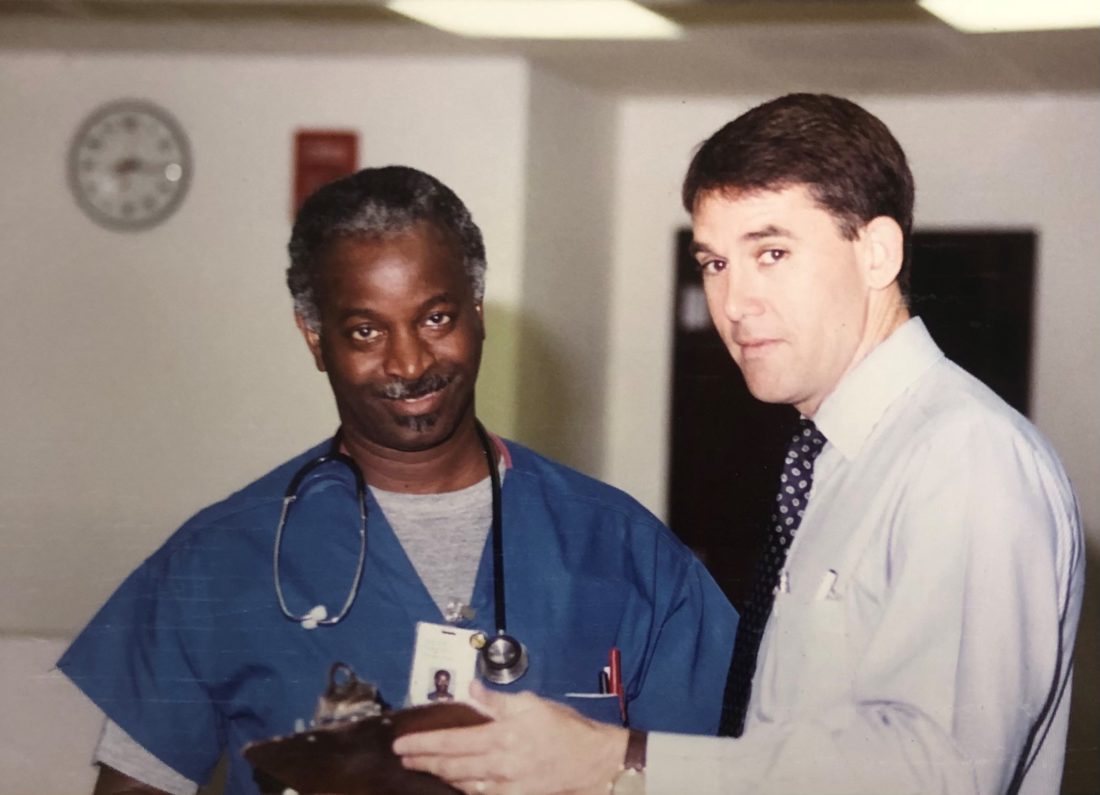 Two men standing in hospital hallway looking at a clipboard. 