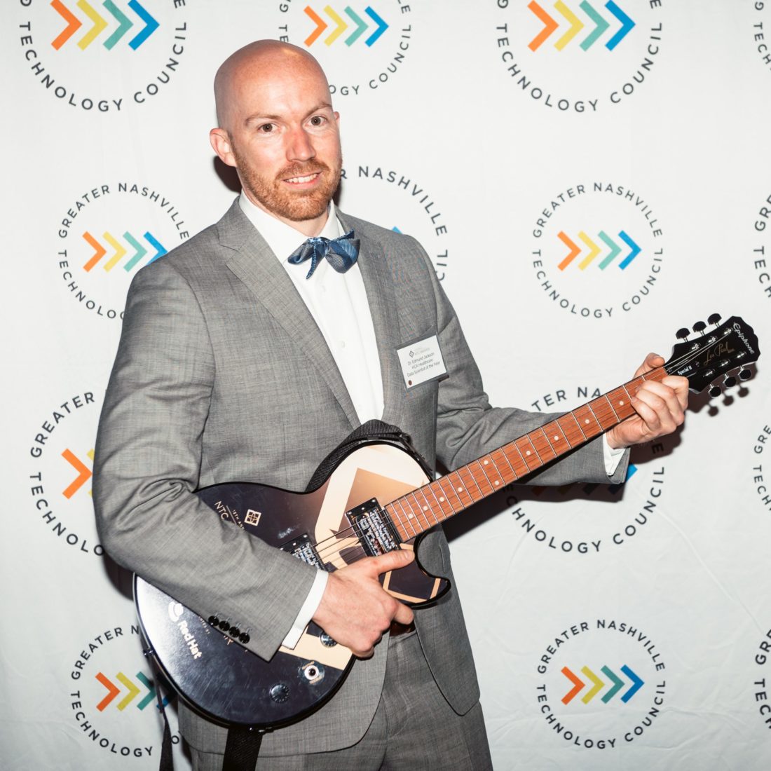 Man wearing suit and bowtie holding an electric guitar. 